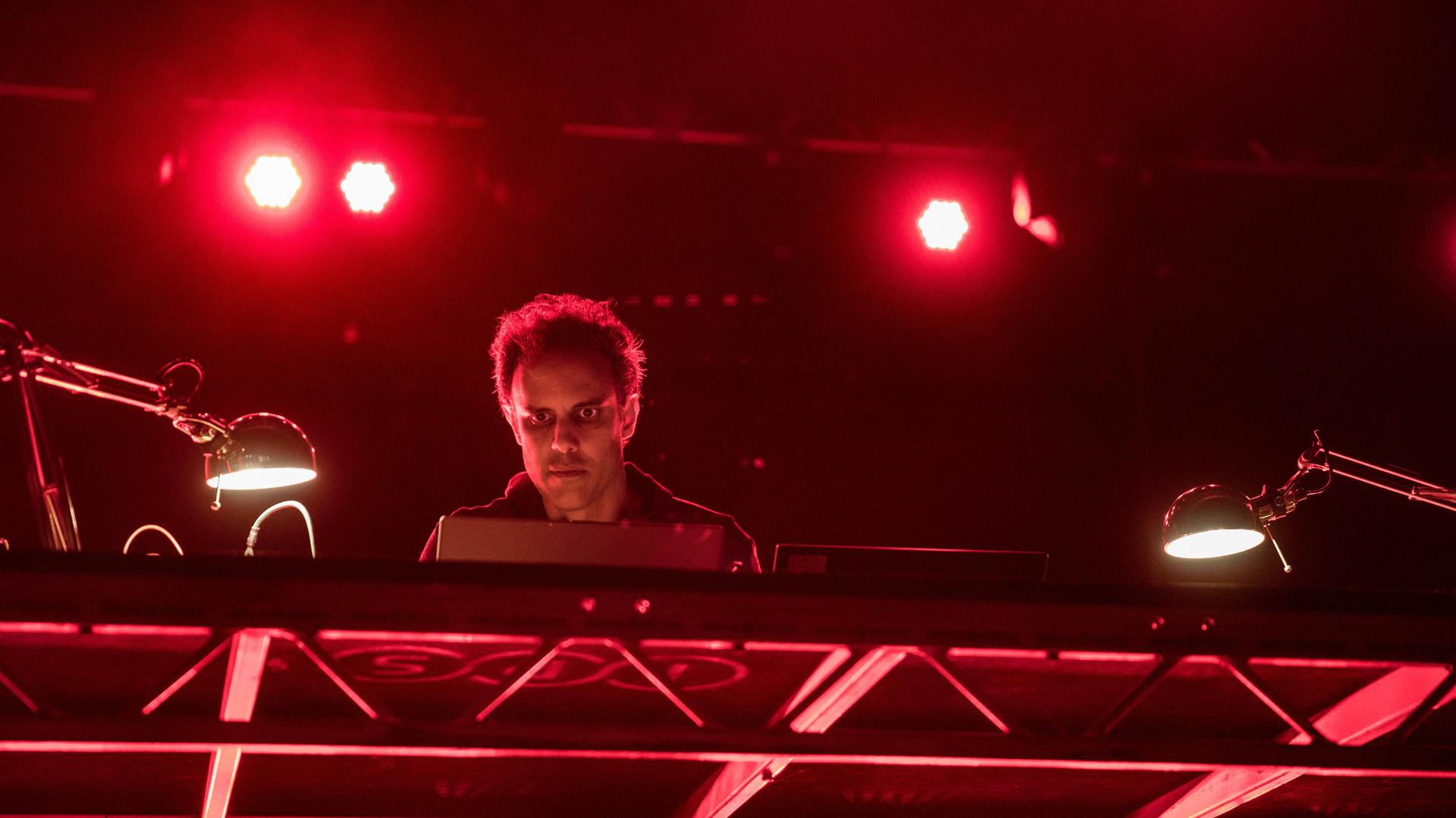 Der Musiker Kieran Hebden, Künstlername Four Tet, auf einer Bühne, angestrahlt von rotem Scheinwerferlicht. Der Musiker Kieran Hebden, Künstlername Four Tet, auf einer Bühne, angestrahlt von rotem Scheinwerferlicht.