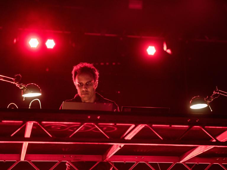 Der Musiker Kieran Hebden, Künstlername Four Tet, auf einer Bühne, angestrahlt von rotem Scheinwerferlicht.