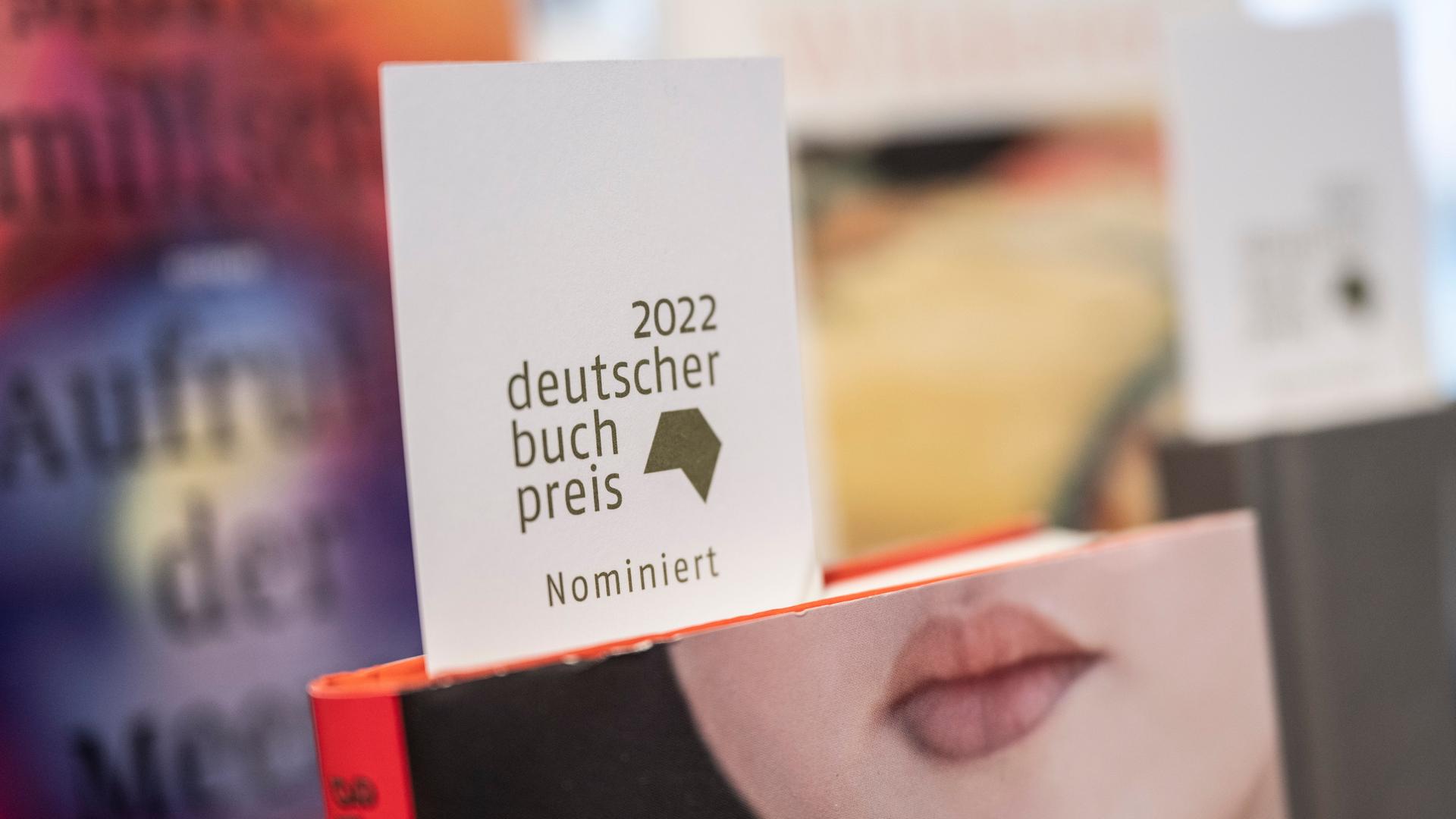 Ein Schild mit der Aufschrift "2022 deutscher Buchpreis nominiert" steckt in der Buchhandlung Bücher im Bogen in Frankfurt am Main in einem Buch mit einem Frauengesicht, bei dem nur der Mund zu sehen  ist.