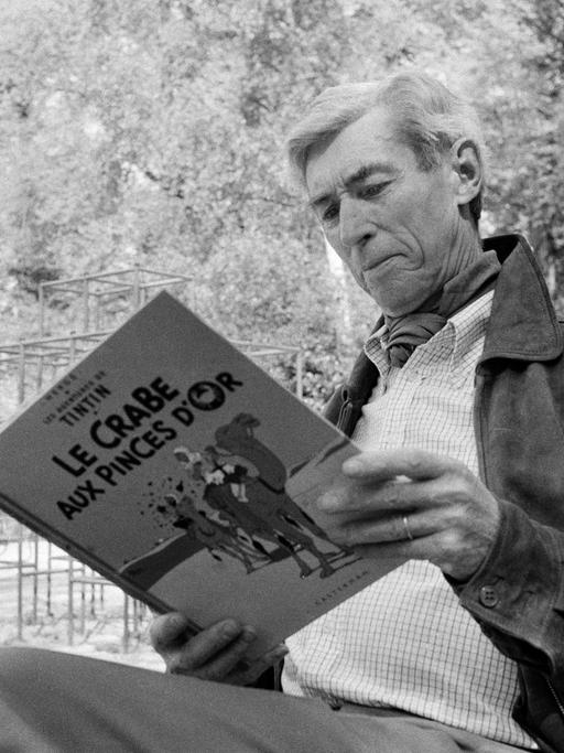 Hergé sitzt mit einer "Tim und Struppi"-Ausgabe in der Hand in einem Garten.
