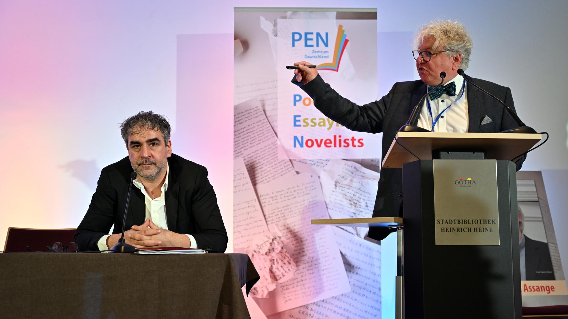 Deniz Yücel und Christoph Nix stehen nebeneinander auf einer Bühne. Nix gestikuliert entrüstet in Yücels Richtung. Deniz Yücel und Christoph Nix stehen nebeneinander auf einer Bühne. Nix gestikuliert entrüstet in Yücels Richtung.