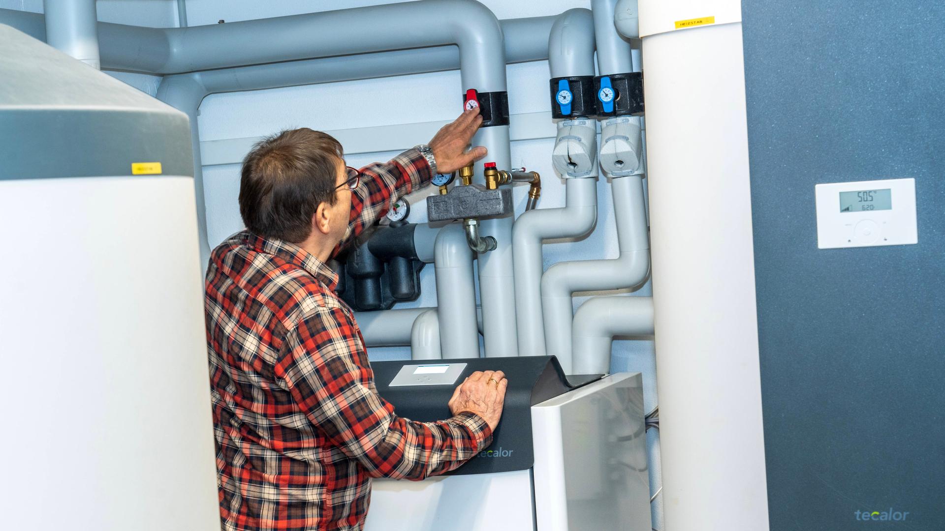 Wärmepumpe in einem Technikraum in einem Privathaus in München. Ein Mann steht vor der Anlage und überprüft die Einstellungen. Wärmepumpe in einem Technikraum in einem Privathaus in München. Ein Mann steht vor der Anlage und überprüft die Einstellungen.