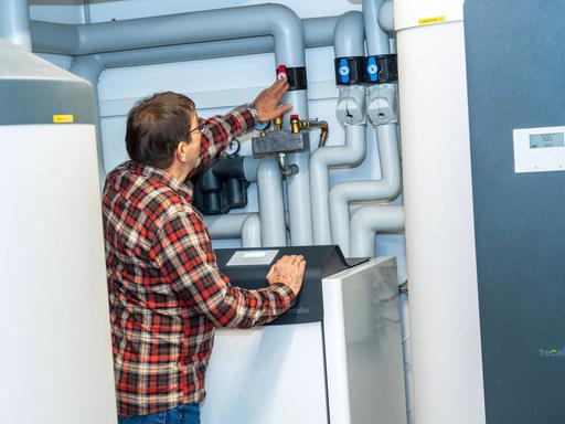 Wärmepumpe in einem Technikraum in einem Privathaus in München. Ein Mann steht vor der Anlage und überprüft die Einstellungen.
