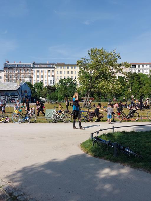 Der Görlitzer Park in Berlin-Kreuzberg bei sommerlichen Temperaturen. Im Vordergrund Besucherinnen und Besucher des Parks, im Hintergrund eine Häuserfront.