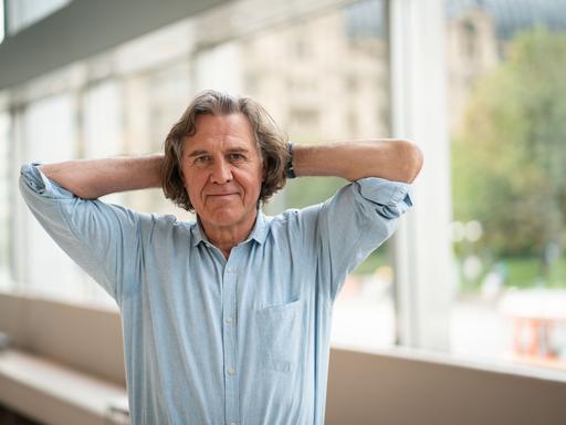 De Krimiautor Norbert Scheuer steht am 29.9.2019 anlässlich der Verleihung des Deutschen Buchpreises im Foyer eines Theaters in Frankfurt. Er trägt ein helles Hemd und hat die Arme hinter dem Kopf verschränkt.