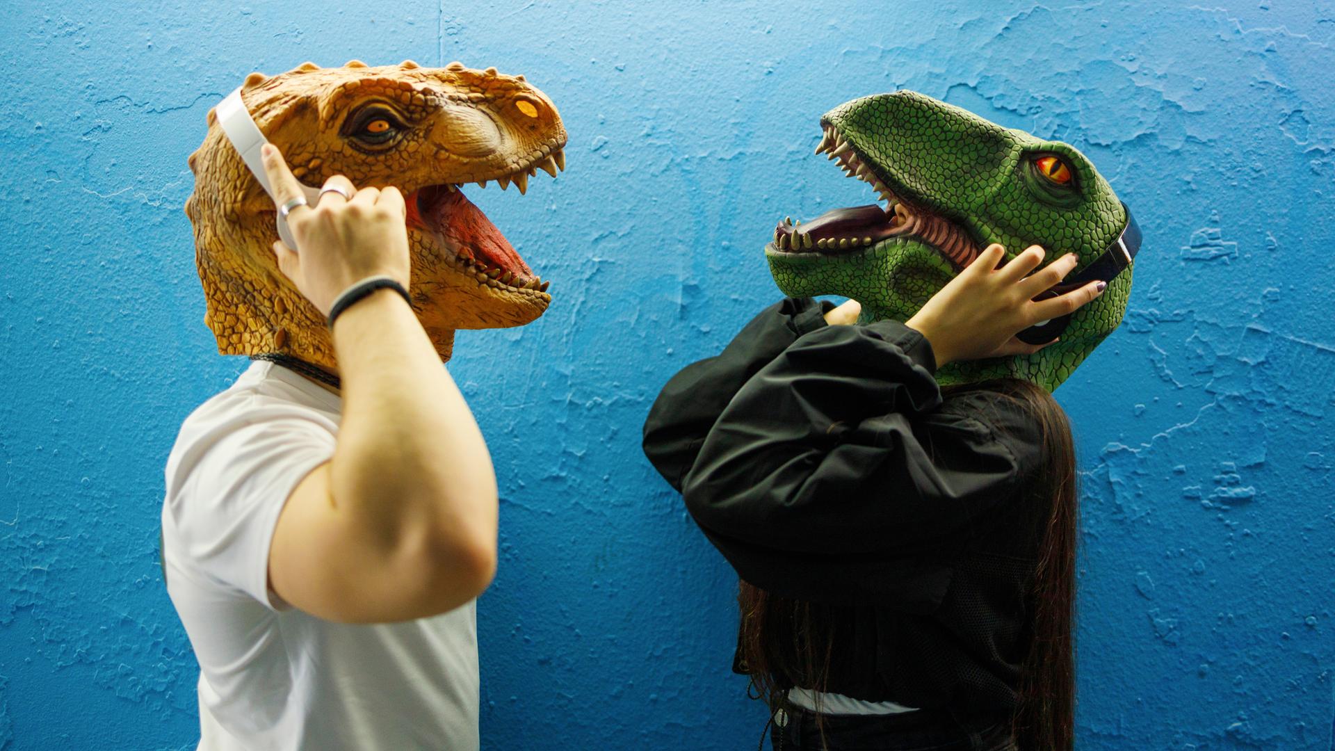 Zwei Menschen mit Dinosauriermaske tragen Kopfhörer und hören Podcasts. Zwei Menschen mit Dinosauriermaske tragen Kopfhörer und hören Podcasts.
