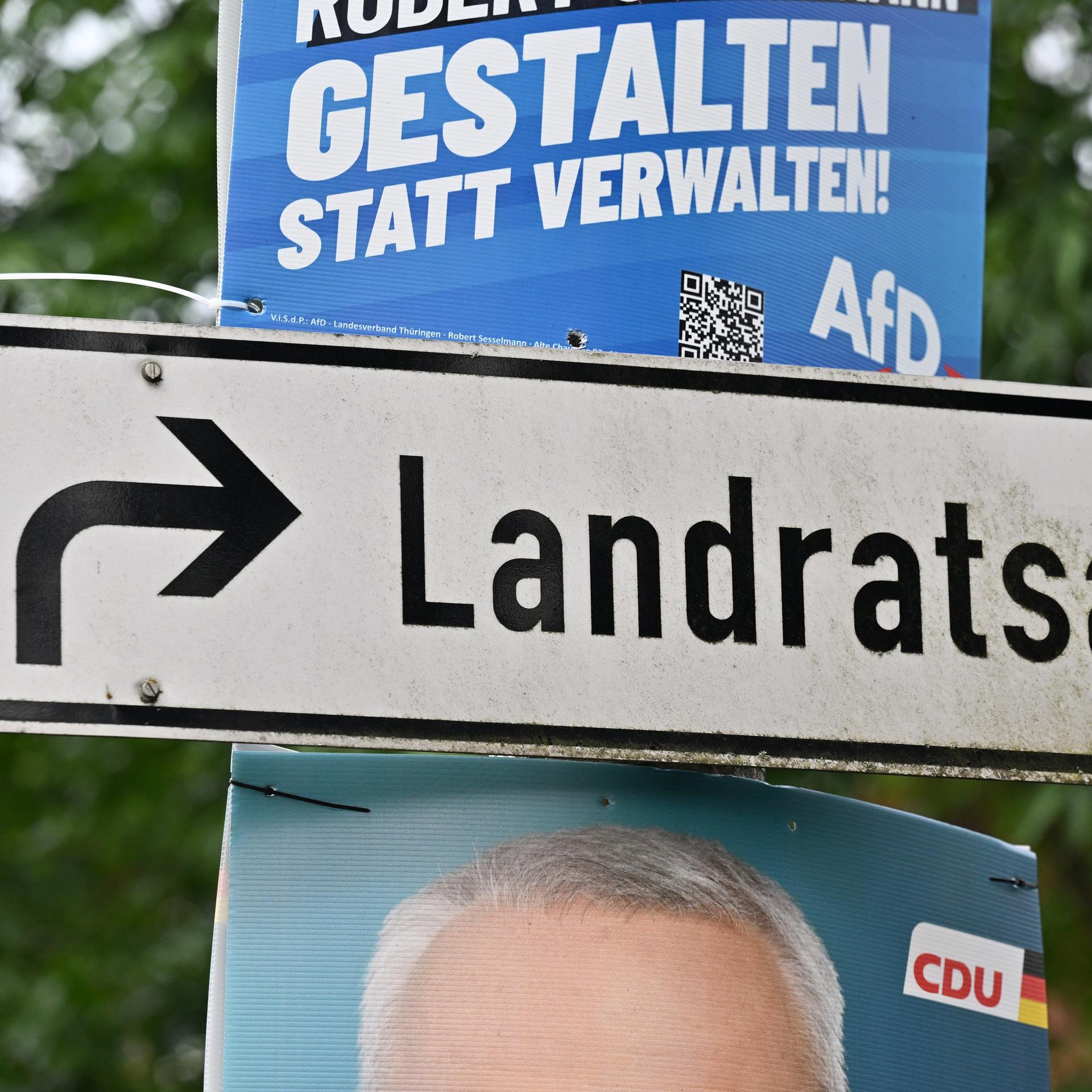 Neben einem Wegweiser zum Landratsamt hängen Plakate mit Fotos der Kandidaten. 