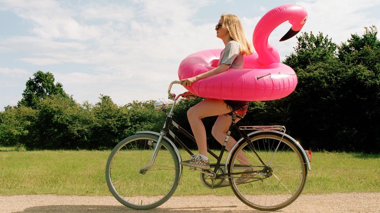 Eine junge Frau auf einem Fahrrad trägt einen aufblasbaren Flamingo um die Hüften.