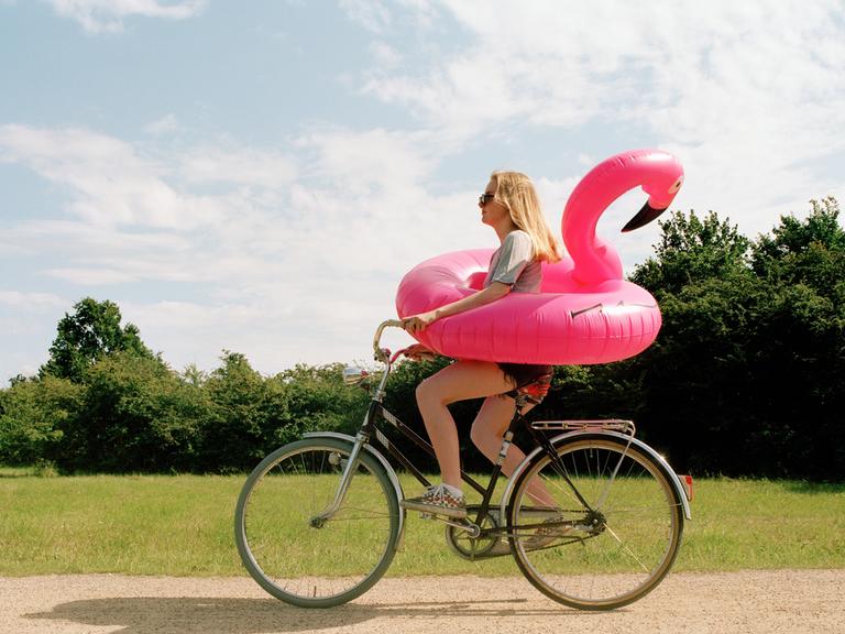 Eine junge Frau auf einem Fahrrad trägt einen aufblasbaren Flamingo um die Hüften.