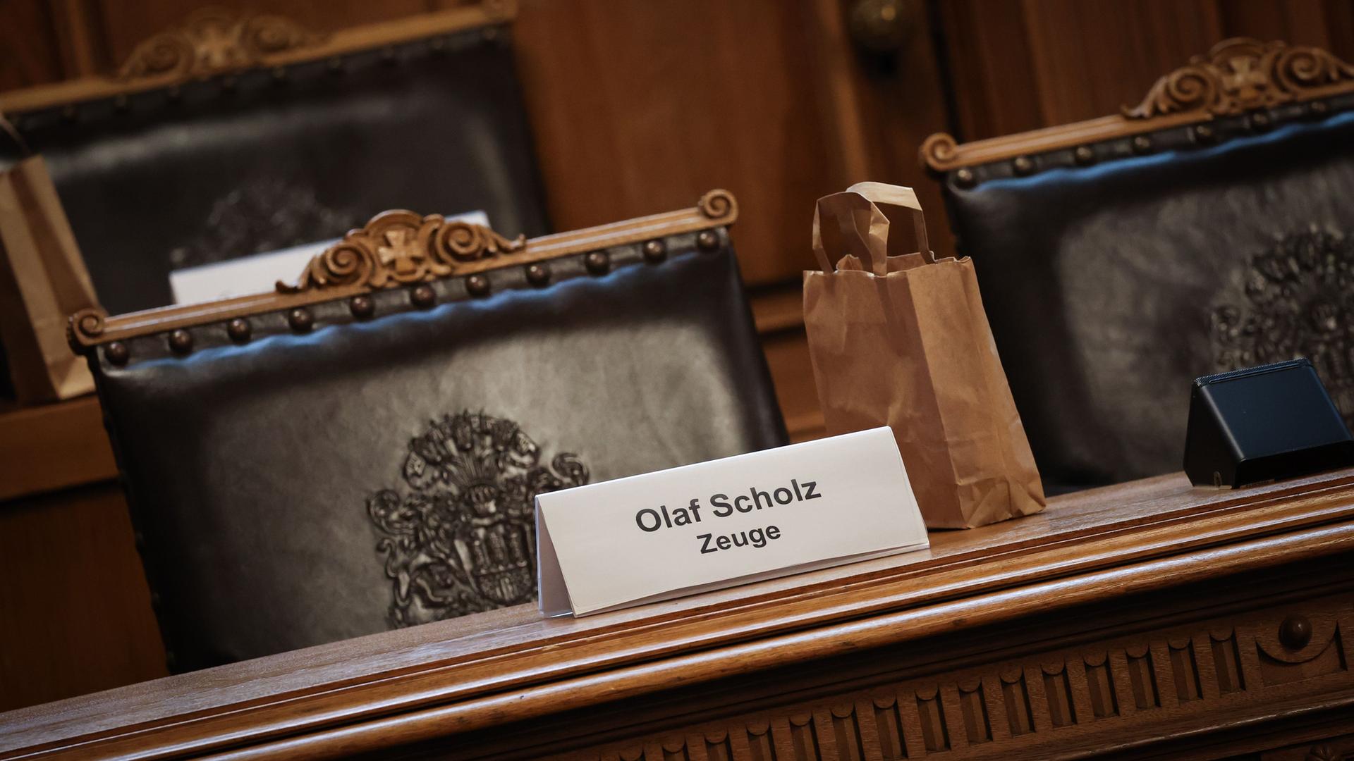 Ein Plastikschild mit dem Text "Olaf Scholz Zeuge" steht auf einem Platz auf der Senatsbank vor Beginn einer Sitzung des Parlamentarischen Untersuchungsausschusses zum Cum-Ex-Komplex Ein Plastikschild mit dem Text "Olaf Scholz Zeuge" steht auf einem Platz auf der Senatsbank vor Beginn einer Sitzung des Parlamentarischen Untersuchungsausschusses zum Cum-Ex-Komplex