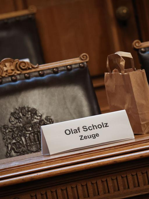Ein Plastikschild mit dem Text "Olaf Scholz Zeuge" steht auf einem Platz auf der Senatsbank vor Beginn einer Sitzung des Parlamentarischen Untersuchungsausschusses zum Cum-Ex-Komplex