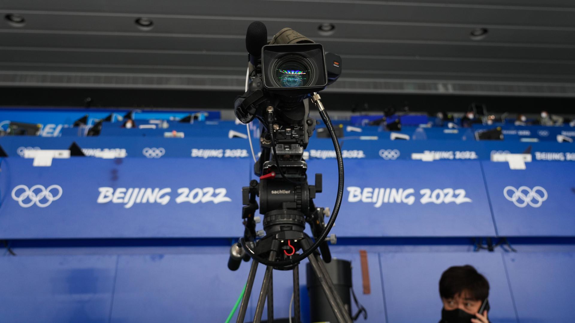 Eine Fernsehkamera steht vor den Logos der Olympischen Winterspiele von Peking 2022