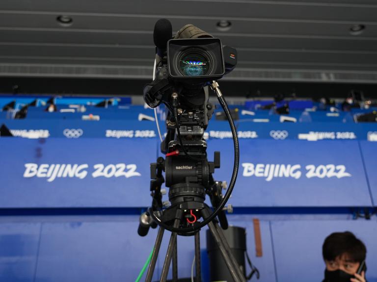 Eine Fernsehkamera steht vor den Logos der Olympischen Winterspiele von Peking 2022