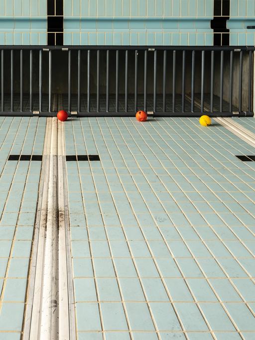 Ein leeres Schwimmbecken mit hellblauen Kacheln und schwarzen Linien.