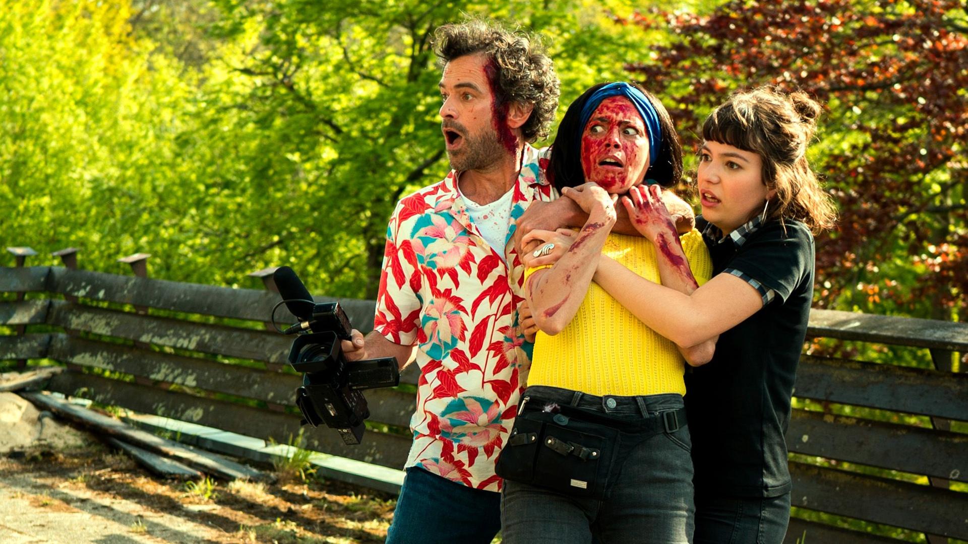 Szene aus dem Eröffnungsfilm der Filmfestspiele von Cannes zeigt eine Gruppe von 3 Personen blutüberströmt und mit erschrockenen Gesichtern. Ein Mann hält eine Kamera in der Hand. Szene aus dem Eröffnungsfilm der Filmfestspiele von Cannes zeigt eine Gruppe von 3 Personen blutüberströmt und mit erschrockenen Gesichtern. Ein Mann hält eine Kamera in der Hand.