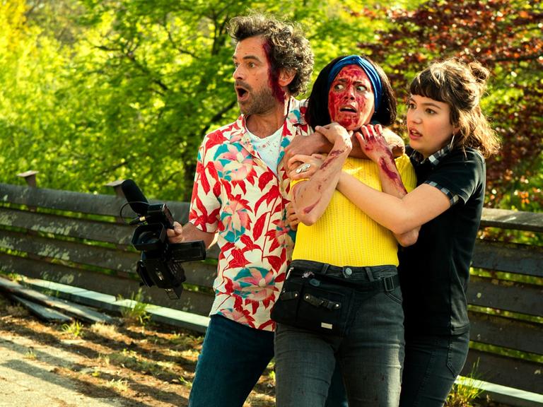 Szene aus dem Eröffnungsfilm der Filmfestspiele von Cannes zeigt eine Gruppe von 3 Personen blutüberströmt und mit erschrockenen Gesichtern. Ein Mann hält eine Kamera in der Hand.