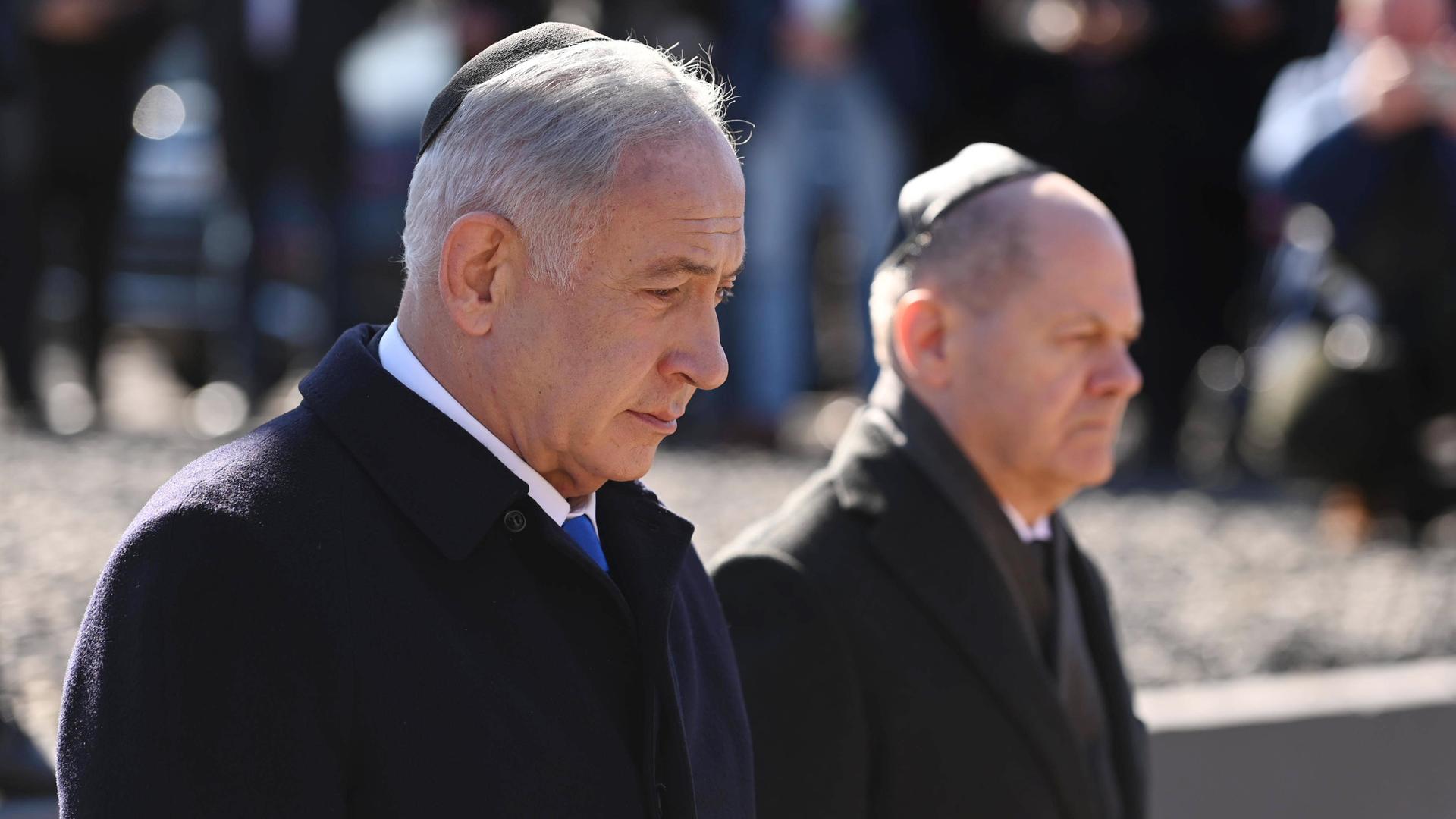 Netanjahu und Scholz besuchen die Gedenk-Stätte "Gleis 17". Sie stehen nebeneinander. Beide tragen eine Kippa. Das ist eine jüdische Kopf-Bedeckung. Netanjahu und Scholz besuchen die Gedenk-Stätte "Gleis 17". Sie stehen nebeneinander. Beide tragen eine Kippa. Das ist eine jüdische Kopf-Bedeckung.