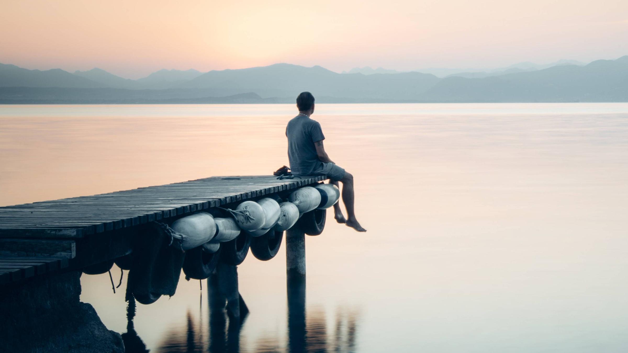 Ein Mensch sitzt am Bootssteg.