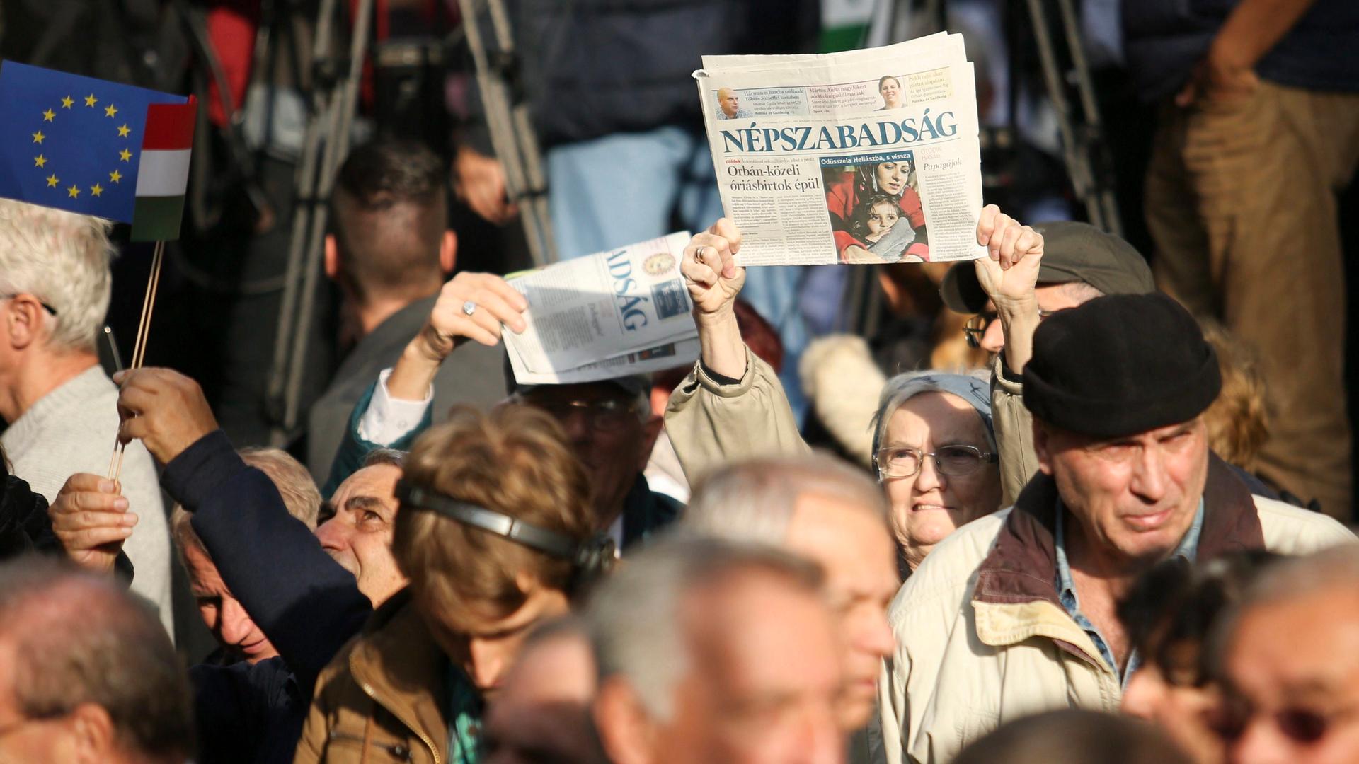 Mitten in einer Gruppe demonstrierender Menschen hält eine Frau eine Zeitung in die Luft.
