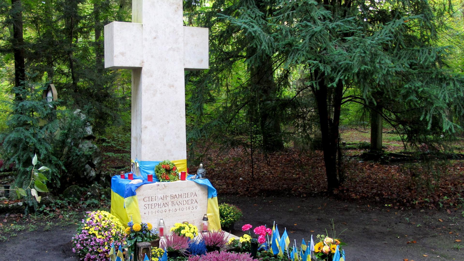 Steinernes Kreuz: Darunter ein mit Blumen und blaugelben Fahnen geschmücktes Grab.