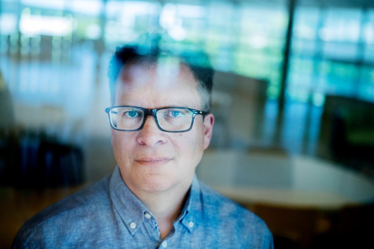 Peter Sjölund. Ein Mann mit Brille steht in einem Raum und schaut durch die Fensterscheibe.