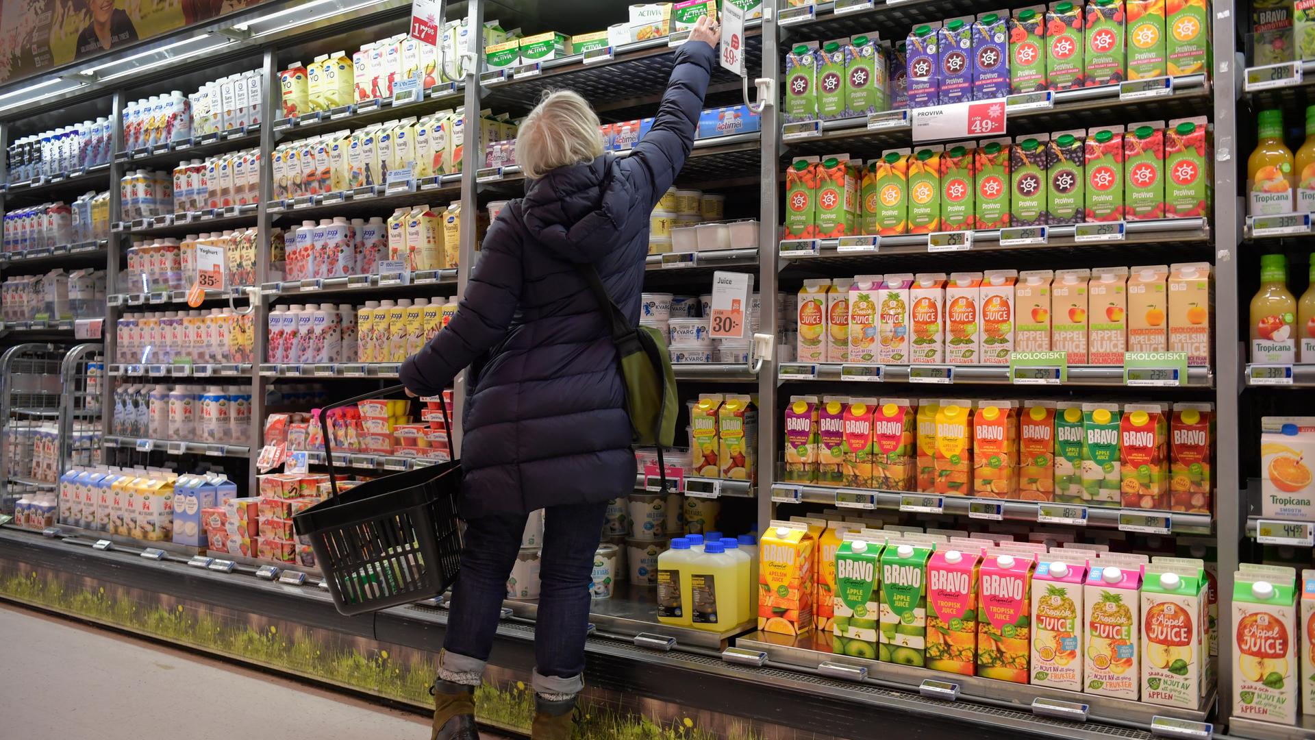 Eine Frau greift im Supermarkt in ein Kühlregal mit Säften Eine Frau greift im Supermarkt in ein Kühlregal mit Säften