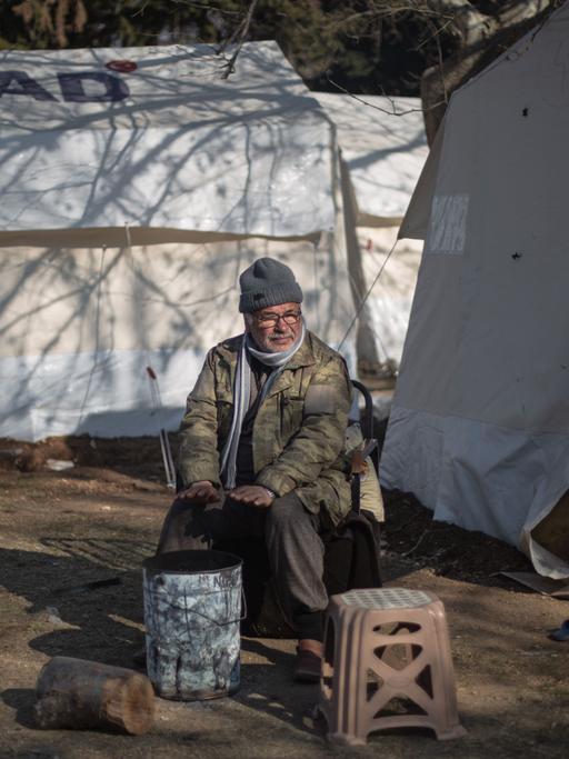 Türkei, Kahramanmaras: Ein Mann sitzt vor seinem Zelt und wärmt sich in einem Behelfslager für Menschen, die ihre Häuser im Epizentrum des Erdbebens verloren haben.