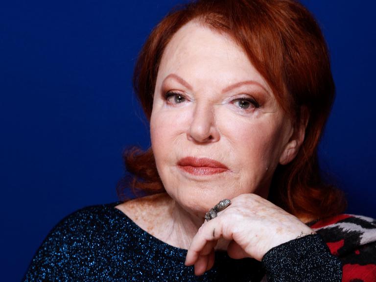 Eine ältere Frau mit rot gefärbten Haaren blickt ernst in die Kamera.