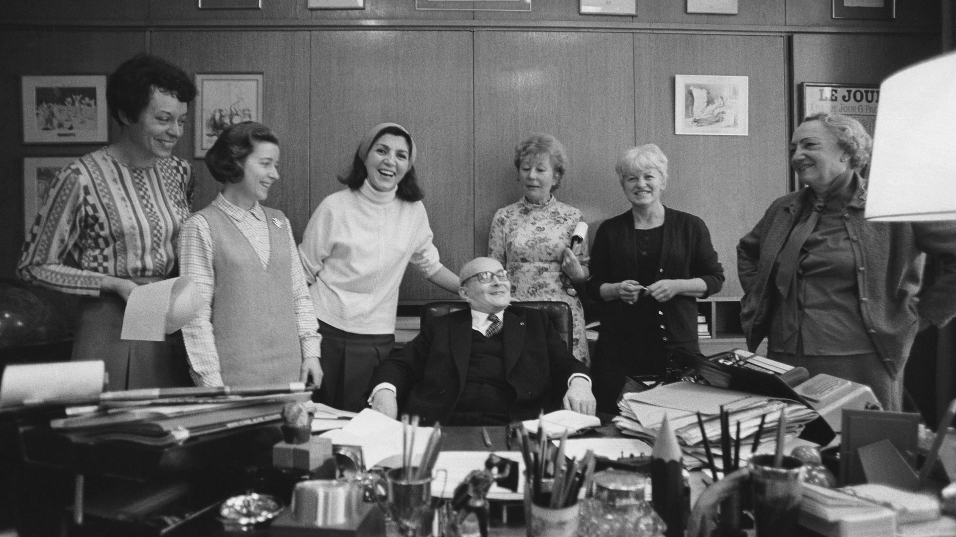 Der französische Journalist Pierre Lazareff sitzt im Jahr 1970 an seinem Schreibtisch, während seine sechs Sekretärinnen ihn umrunden.
