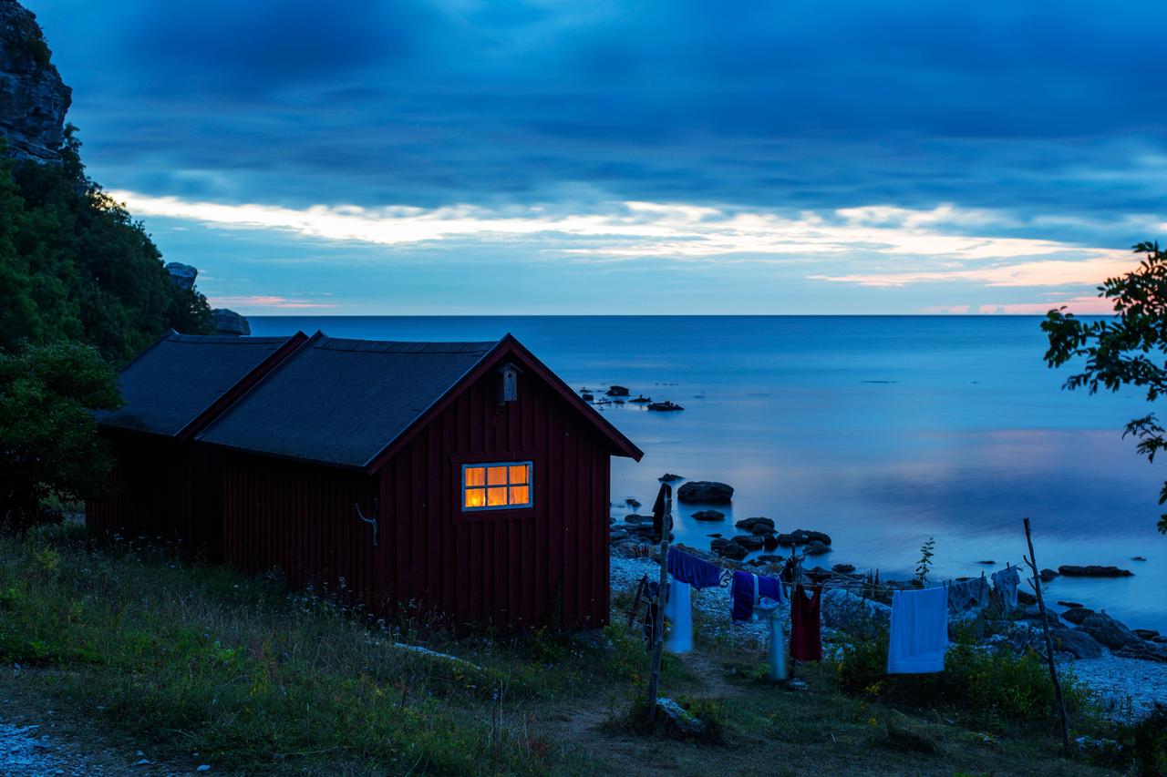 In einer Holzhütte am Ufer brennt in der Abenddämerung Licht, Wäsche hängt auf der Leine über der Wiese. In einer Holzhütte am Ufer brennt in der Abenddämerung Licht, Wäsche hängt auf der Leine über der Wiese.