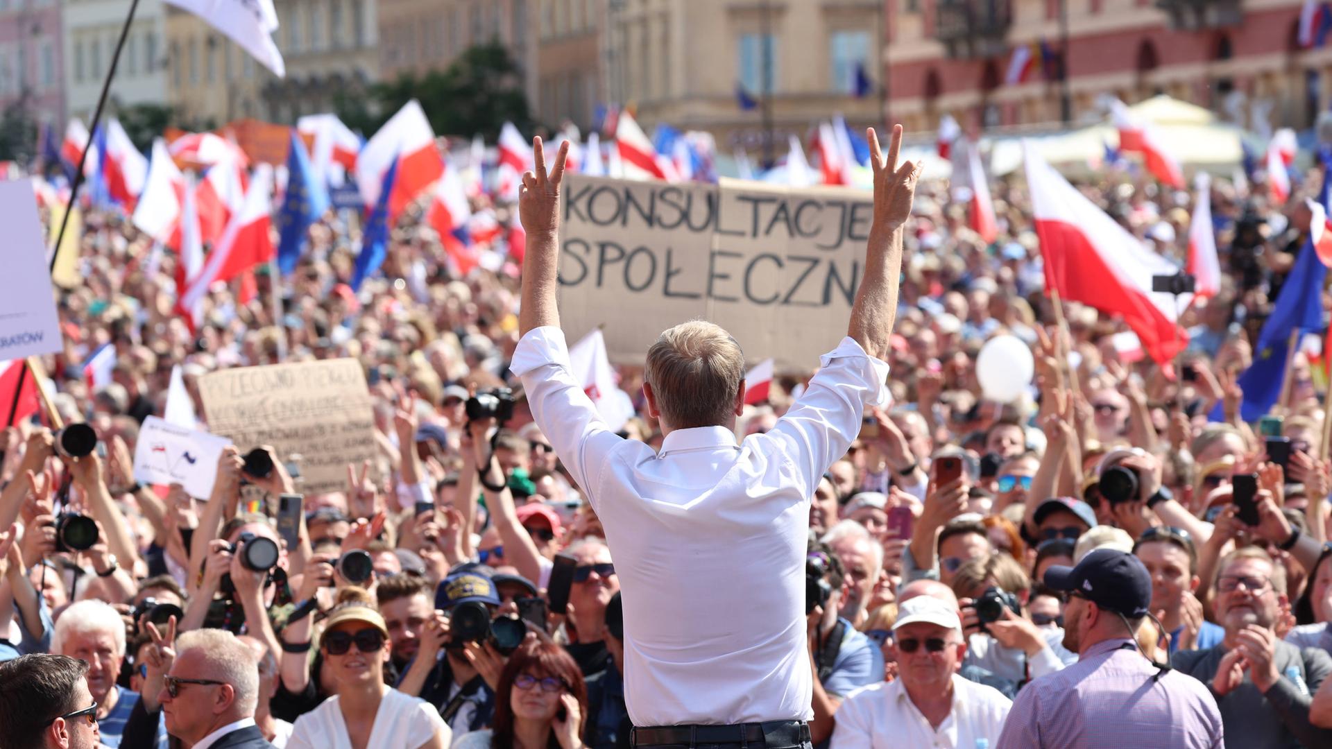 Oppositionspolitiker Donald Tusk steht mit erhobenen Armen in Warschau vor den Teilnehmenden der Großdemonstration gegen die Politik der nationalkonservativen Regierungspartei PiS.