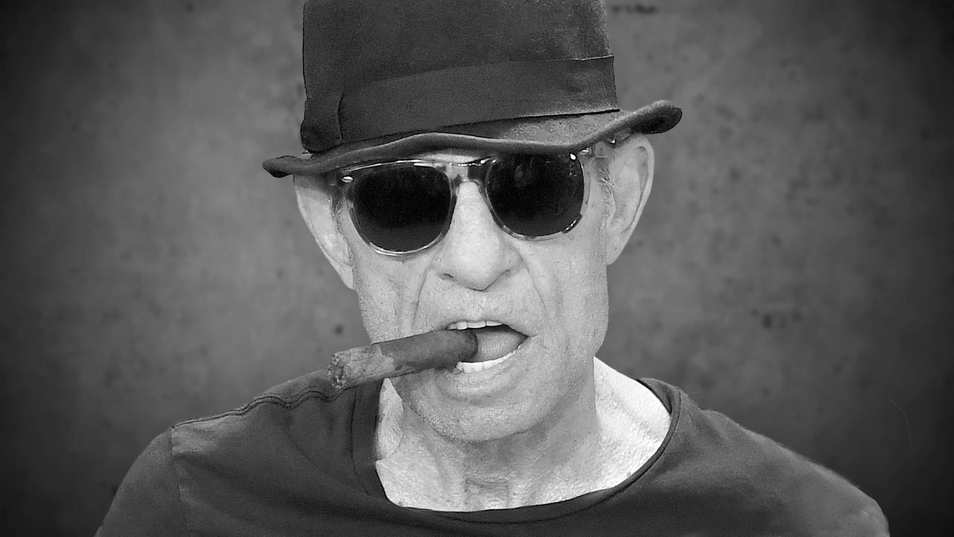 Porträt von Regisseur Klaus Lemke mit einer Zigarre im Mundwinkeln und Hut. Porträt von Regisseur Klaus Lemke mit einer Zigarre im Mundwinkeln und Hut.