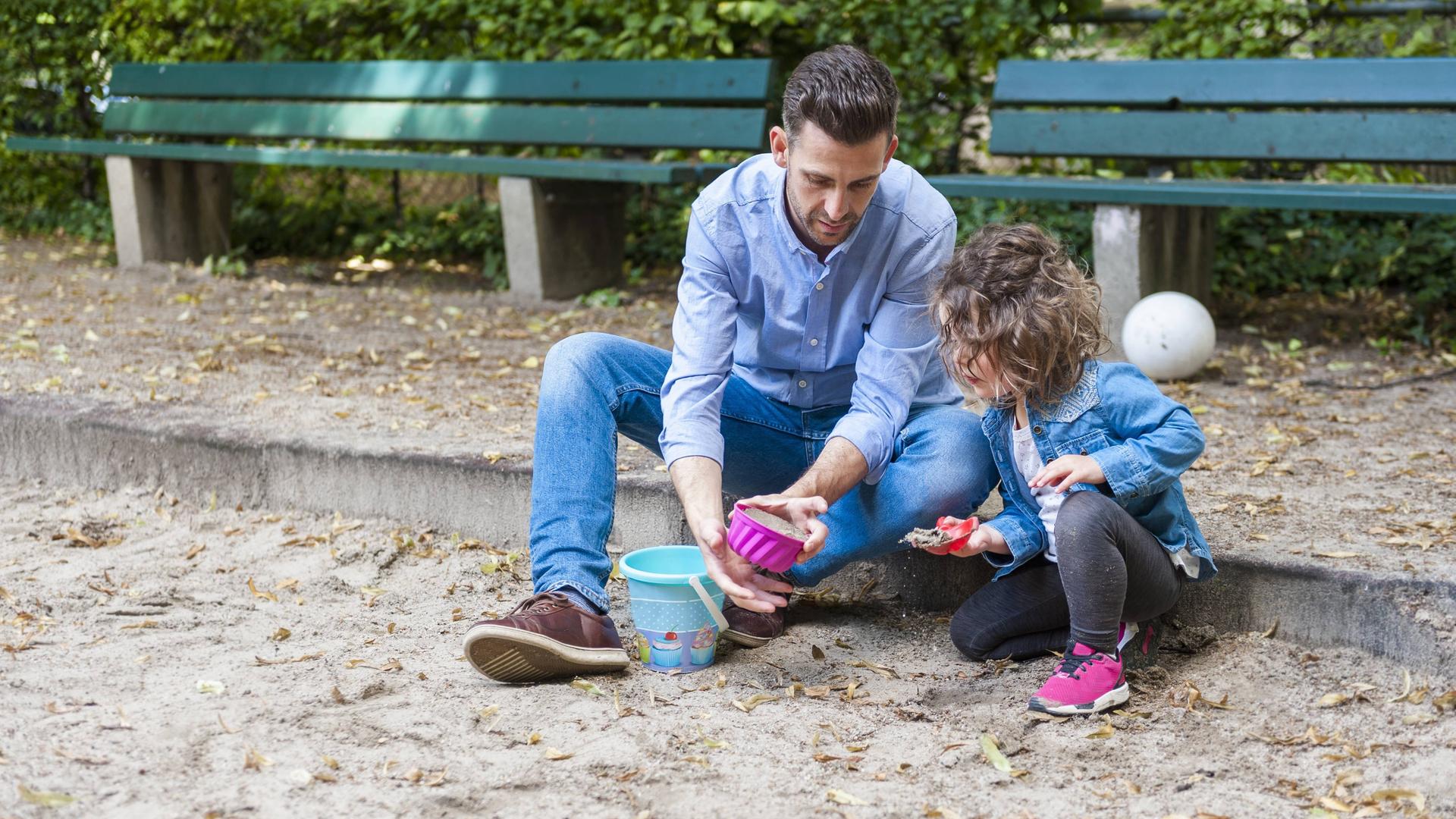 Ein Vater spielt mit seiner kleinen Tochter im Sandkasten auf einem Spielplatz Ein Vater spielt mit seiner kleinen Tochter im Sandkasten auf einem Spielplatz