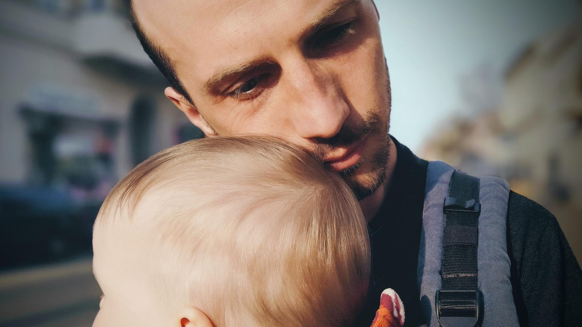 Ein junger Vater mit seinem Sohn im Babyalter. Er legt seine Wange an den Kinderkopf.. 