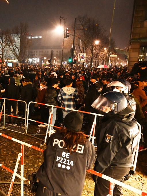 Polizisten stehen hinter einer Absperrung am Brandenburger Tor in Berlin, wo sich mehrere hundert Menschen versammelt haben (aufgenommen in der Silvesternacht zum Jahreswechsel 2022/2023) 