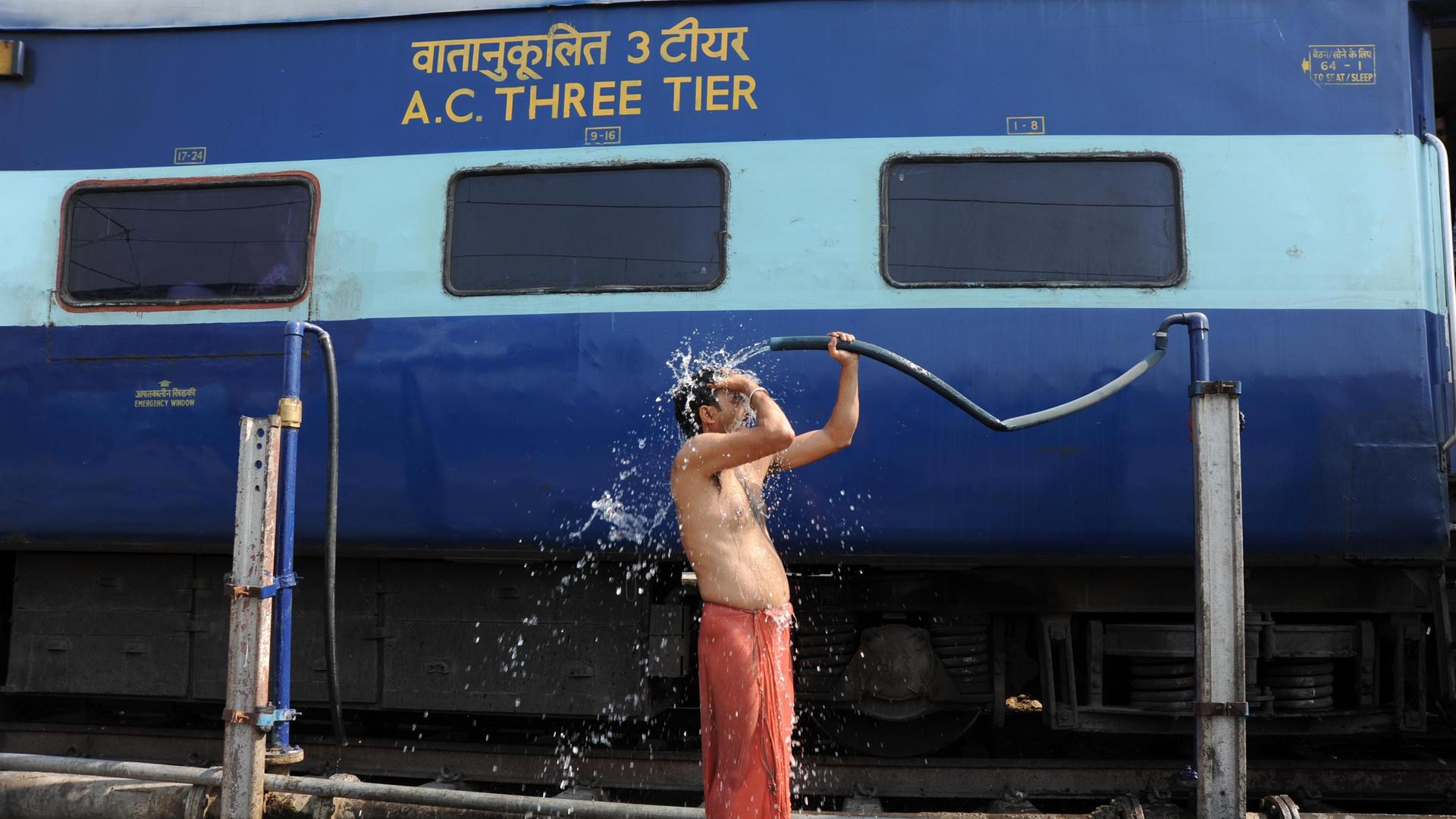 Ein Bahnreisender begießt sich in Allahabad, Uttar Pradesh, Indien neben einem Zug mit Wasser. Ein Bahnreisender begießt sich in Allahabad, Uttar Pradesh, Indien neben einem Zug mit Wasser.