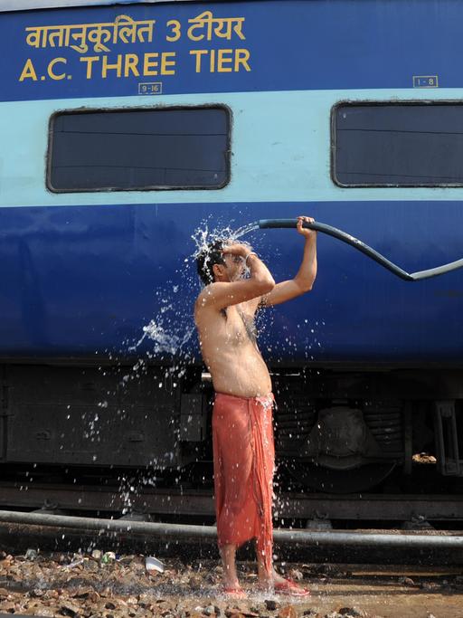 Ein Bahnreisender begießt sich in Allahabad, Uttar Pradesh, Indien neben einem Zug mit Wasser.
