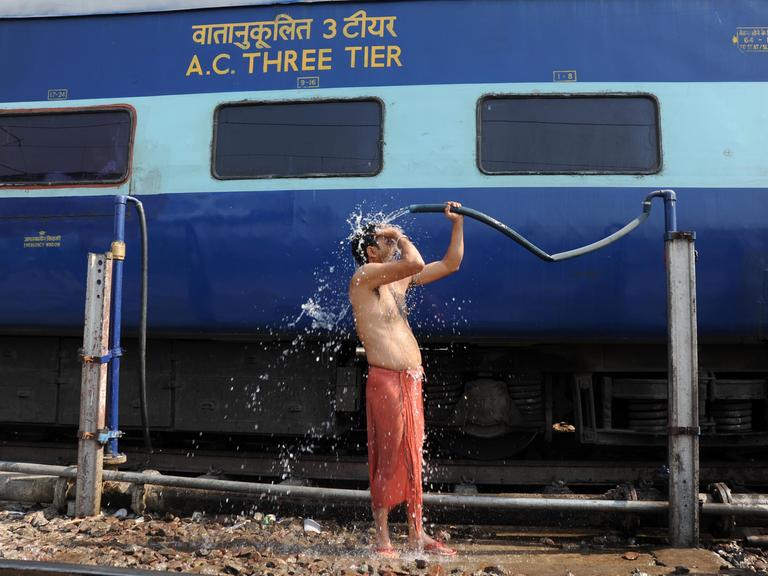 Ein Bahnreisender begießt sich in Allahabad, Uttar Pradesh, Indien neben einem Zug mit Wasser.
