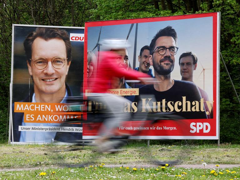 Wahlplakate mit Portraits der nordrhein-westfälischen Spitzenkandidaten von CDU, Ministerpräsident Hendrik Wüst (l), und SPD, Thomas Kutschaty (r), stehen auf einer Wiese. In Nordrhein-Westfalen findet am 15. Mai 2022 die Landtagswahl statt.