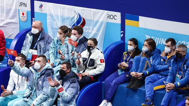Russische und ukrainische Sportlerinnen und Sportler sitzen beim Eiskunstlaufwettkampf in Peking direkt nebeneinander.  