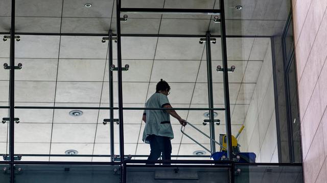 In einem Bürogebäude arbeitet eine Putzfrau hinter einer Glaswand. 