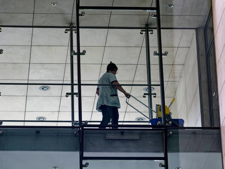 In einem Bürogebäude arbeitet eine Putzfrau hinter einer Glaswand. 
