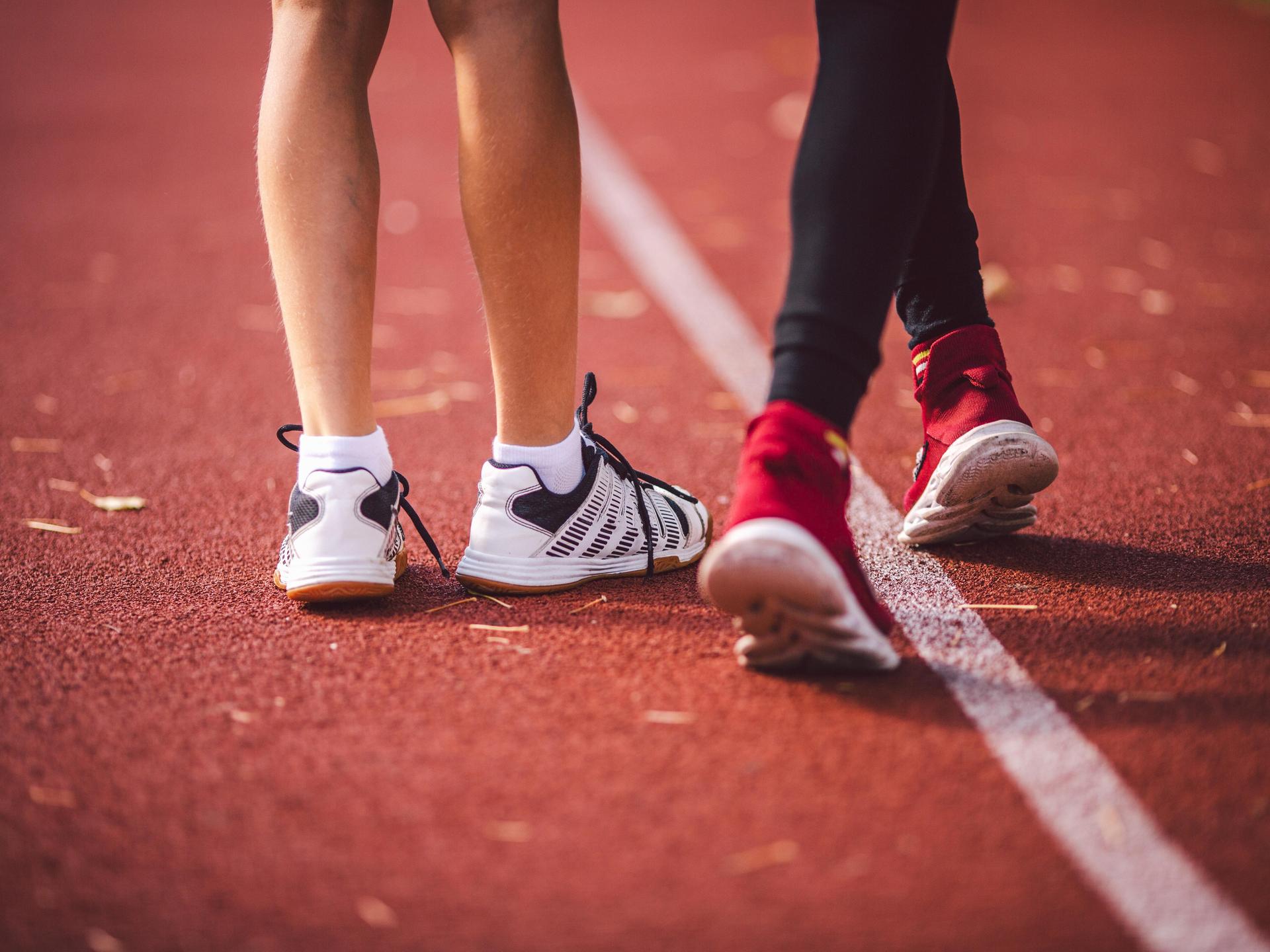 Die Beine zweiter Kinder in Sportschuhen und Sportbekleidung auf einem Sportplatz