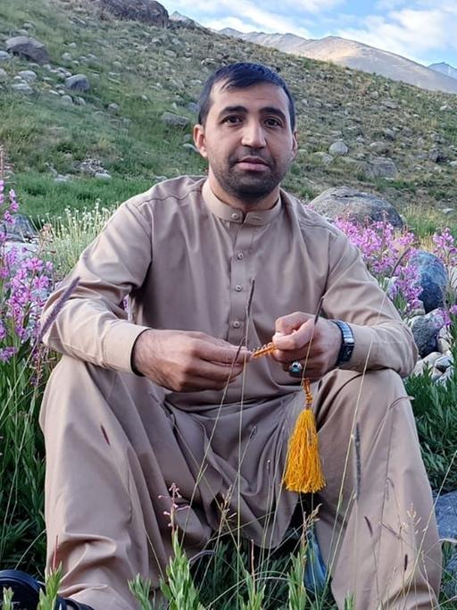 Der Übersetzer Jawed Haqmal in Afghanistan vor einer blühenden Wiese mit einer Berglandschaft im Hintergrund. 