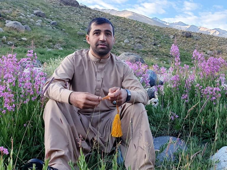 Der Übersetzer Jawed Haqmal in Afghanistan vor einer blühenden Wiese mit einer Berglandschaft im Hintergrund. 