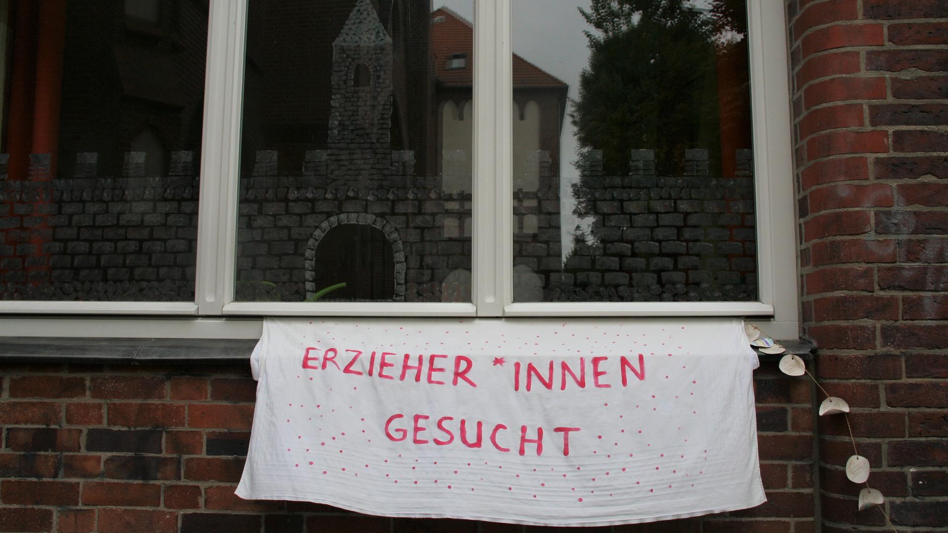 Ein Transparent auf dem geschrieben steht, "Erzieher*innen gesucht" an einer Häuserwand aus Backstein in Berlin. Ein Transparent auf dem geschrieben steht, "Erzieher*innen gesucht" an einer Häuserwand aus Backstein in Berlin.