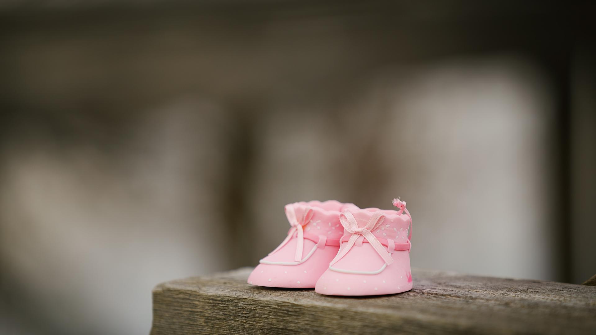Ein rosa farbenes Paar Babyschuhe steht auf einem Holzregal. Ein rosa farbenes Paar Babyschuhe steht auf einem Holzregal.