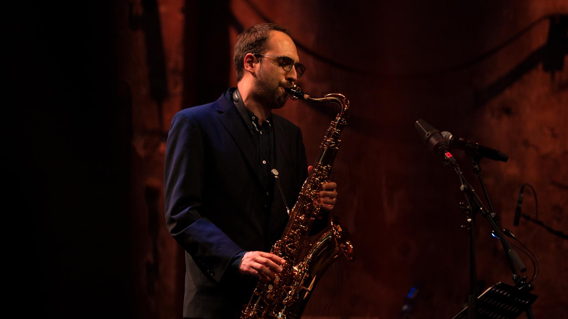 Ein junger Mann mit braunen Haaren und Brille spielt auf einem Saxofon. Ein junger Mann mit braunen Haaren und Brille spielt auf einem Saxofon.