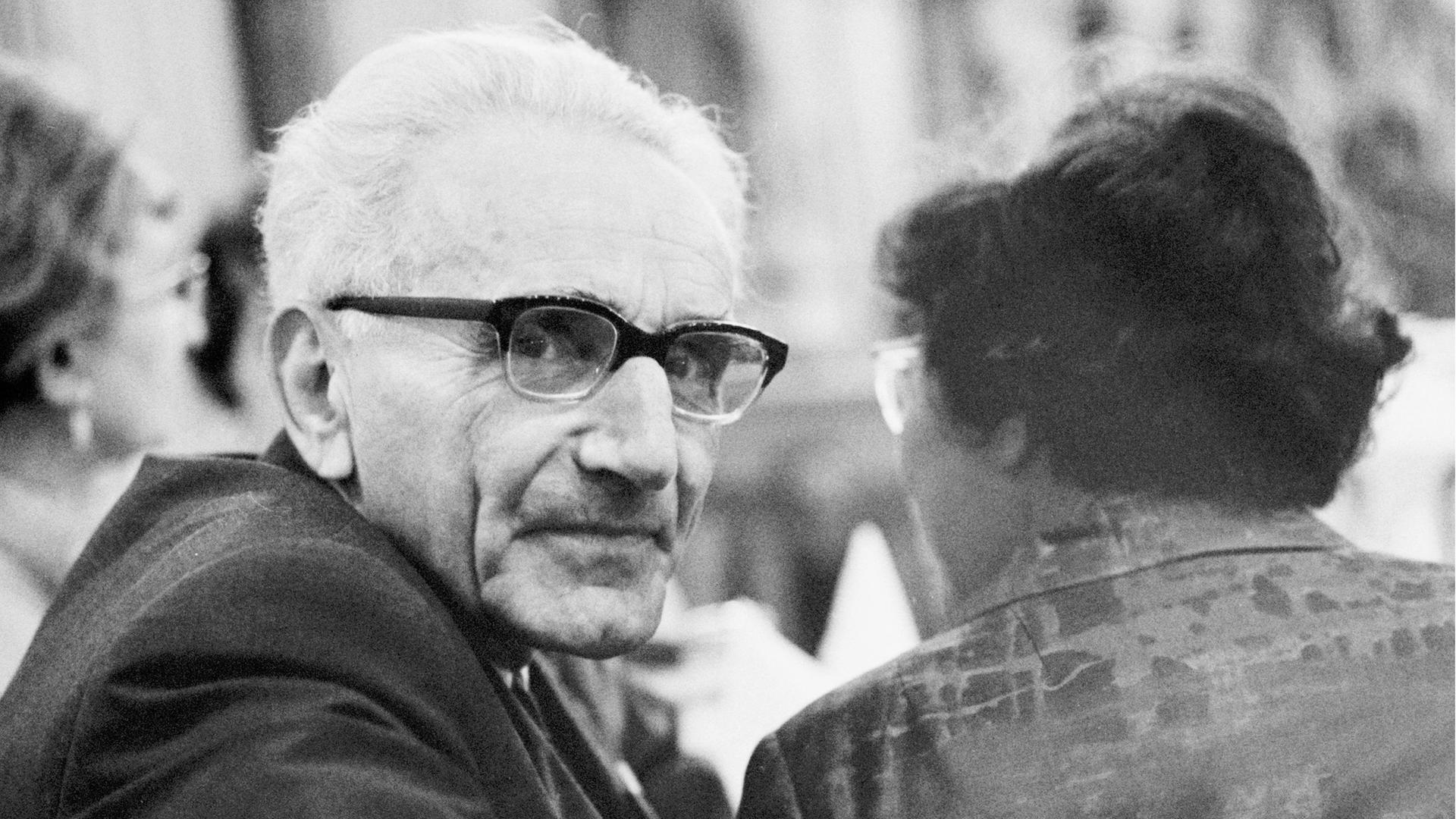 Schwarzweißfoto von Günther Anders mit weißem Haar und dicker Brille, der sich auf einem Stuhl sitzend zur Kamera umdreht. Schwarzweißfoto von Günther Anders mit weißem Haar und dicker Brille, der sich auf einem Stuhl sitzend zur Kamera umdreht.