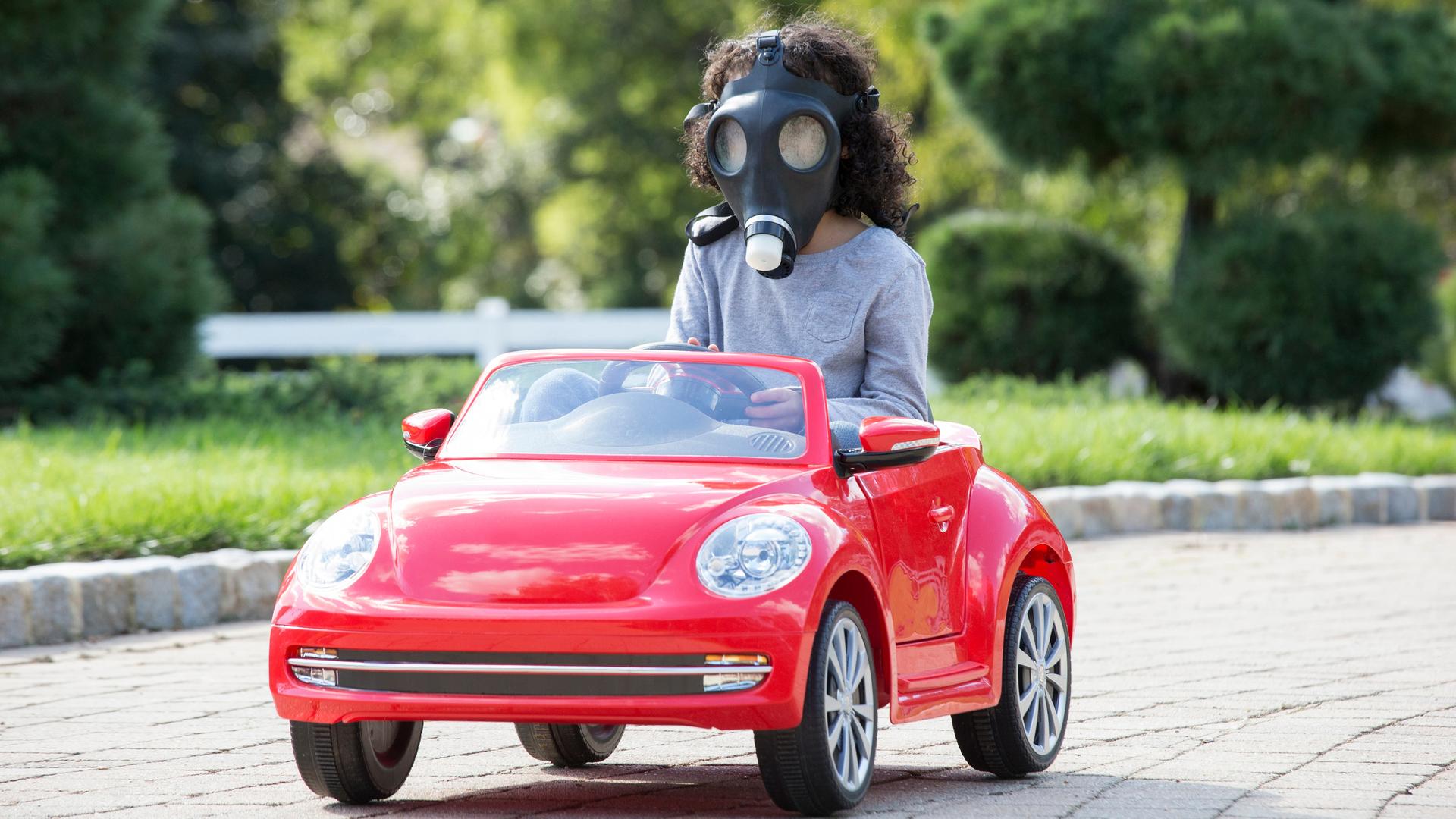 Ein Kind mit einer Gasmaske führt mit einem roten Spielzeugauto. Ein Kind mit einer Gasmaske führt mit einem roten Spielzeugauto.